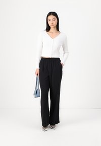 White ribbed cropped cardigan with V-neck and buttons, paired with black elastic-waist wide-leg trousers and a small blue handbag.