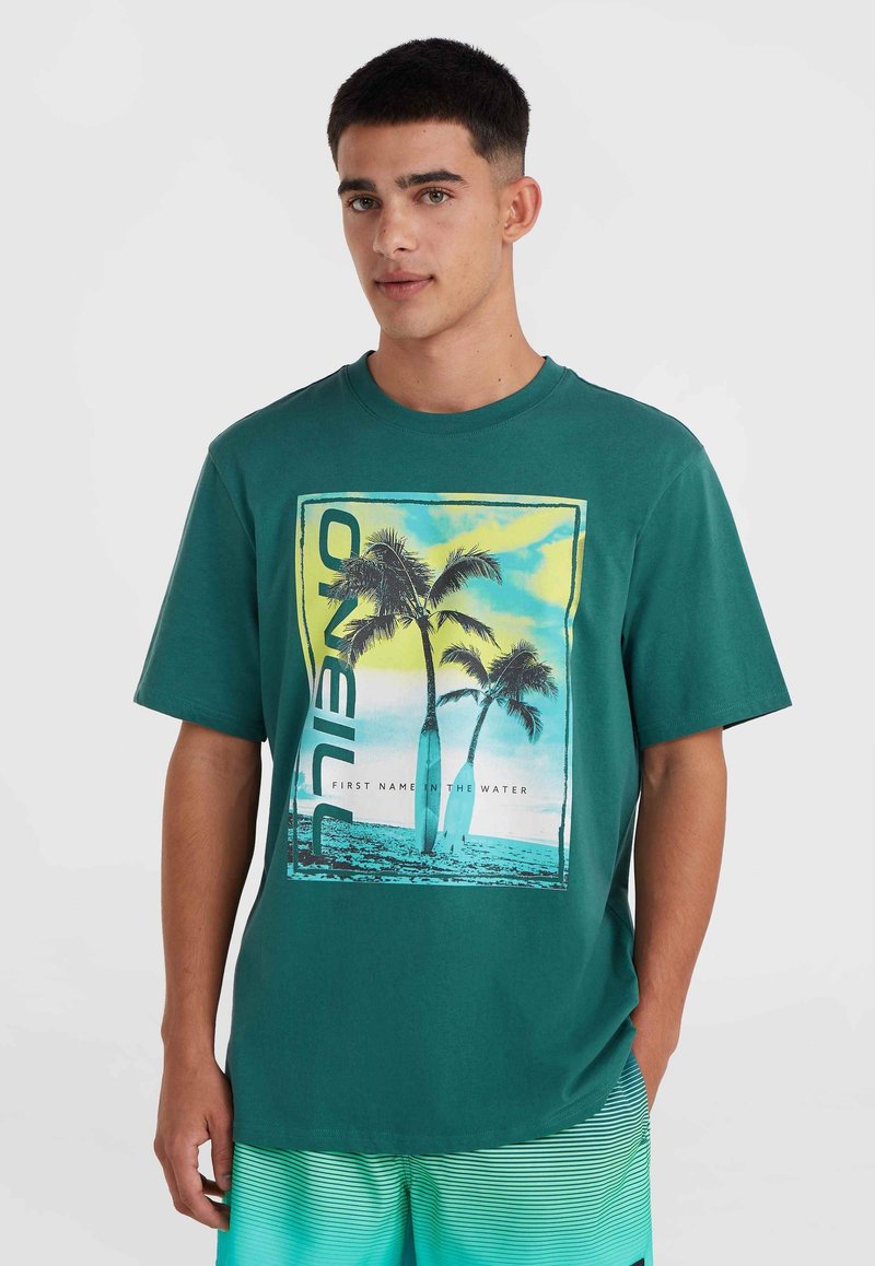 Camiseta de manga corta en color azul claro con un diseño gráfico tropical que incluye palmeras, texto enmarcado y un fondo colorido. Material de algodón suave.