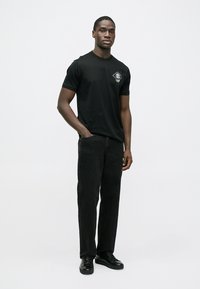 Μαύρο βαμβακερό t-shirt με στρογγυλή λαιμόκοψη και κοντά μανίκια, διακοσμημένο με ένα μικρό τυπωμένο λογότυπο στο αριστερό στήθος. Συνδυάζεται με μαύρα τζιν και αθλητικά παπούτσια.