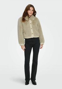 Cropped faux fur jacket in light beige with a plush texture, featuring a button front and a soft collar. Worn with black flared pants.