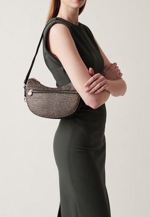 Borsa a spalla texturizzata, nera e beige, con forma curvata, chiusura a zip e una sottile tracolla regolabile, indossata accanto a un modello in un vestito verde.