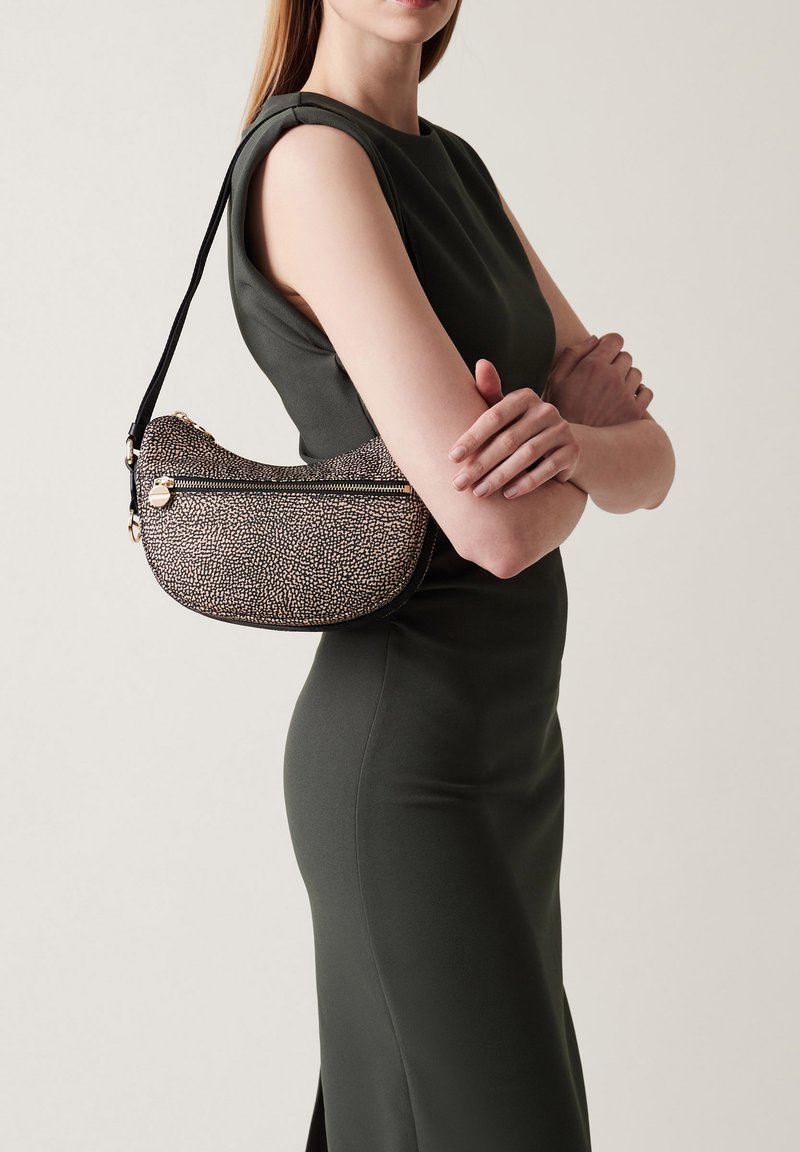 Sac à épaule texturé, noir et beige, de forme courbée, avec une fermeture éclair et une fine sangle réglable, porté à côté d'un mannequin en robe verte.