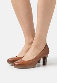 Escarpins en cuir marron à talons hauts avec un bout rond, texture lisse et un talon en bois empilé, présentant un design de cou-de-pied échancré.