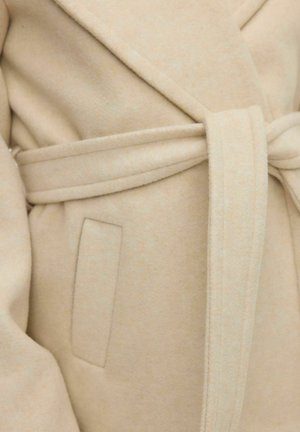 Beige vilnas maisījuma mētis ar apvīšanas dizainu, piedāvājot sasietu jostu, strukturētu apkakli un sānu kabatu. Mīksta tekstūra, minimālisma stils.