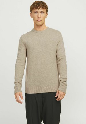 Beige knitted sweater with a round neck, ribbed cuffs, and hem. Soft texture, long sleeves, standard fit. Worn over black trousers.