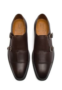 Hnědé kožené boty s špičatou špičkou, dvojitým přezkovým akcentem a texturovanou podrážkou. Obsahují vyražené logo uvnitř.