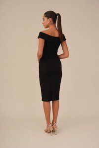 Zwarte off-shoulder jurk met een getailleerde silhouette, knielange zoom, ritssluiting aan de achterkant en een split; gedragen met gouden sandalen met bandjes.