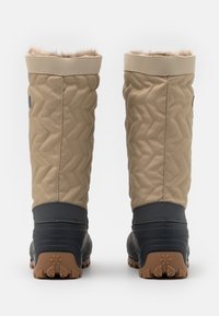 Bottes imperméables matelassées beiges avec un col en fausse fourrure, semelles en caoutchouc noir et motif de grip texturé, conçues pour une utilisation en extérieur.
