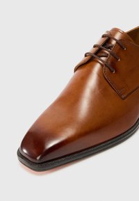 Zapato de vestir de piel marrón con un acabado suave, punta afilada y cordones marrones. Presenta costuras decorativas a lo largo de la suela.