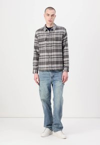 Grå og hvit rutete flanellskjorte med to frontlommer, sammen med lyseblå jeans og hvite joggesko. Glatt stoff og avslappet passform.