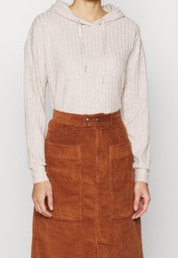 Sudadera beige con textura en relieve y cordones, combinada con una falda de pana de color óxido con cintura alta y dos bolsillos frontales de parche.