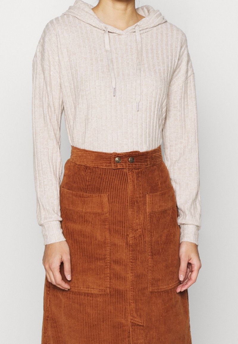 Sudadera beige con textura en relieve y cordones, combinada con una falda de pana de color óxido con cintura alta y dos bolsillos frontales de parche.