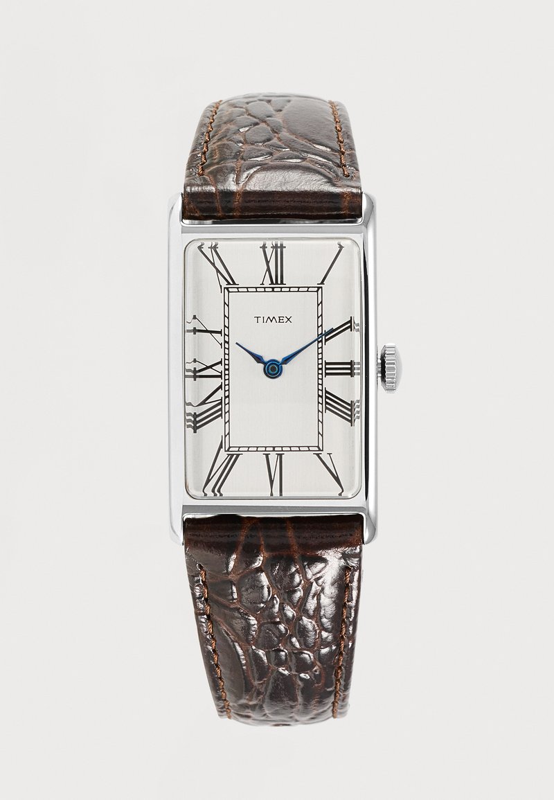 Montre Timex rectangulaire argentée avec cadran blanc, chiffres romains noirs, aiguilles bleues et bracelet en cuir brun foncé texturé.