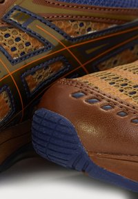 Bruna sportskor med en kombination av texturerad mesh och slät läder, med marinblå accenter och intrikata sömnadsdetaljer.