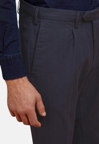 Pantalon bleu marine à taille plate en mélange de coton ; présente une coupe slim, des passants de ceinture et des poches latérales, avec une texture lisse et un léger éclat.