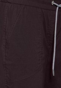 Dunkelviolette Shorts aus leichtem Stoff mit einem Kordelzug, Seitentaschen und einem kontrastierenden Kordelzug in schwarz-weißen Streifen.