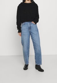 Black knitted sweater with wide collar, paired with light blue high-waisted straight jeans. Black ankle boots complete the outfit.