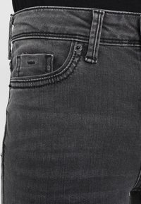 Černé denimové džíny se klasickým pěti kapsovým designem, se švy a detaily na knoflíkovém zapínání. Jemně vybledlá textura po celém materiálu.