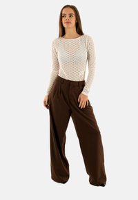 Top a maniche lunghe di colore crema con motivo, abbinato a pantaloni ampi a vita alta di colore marrone. Texture liscia con un fit comodo.