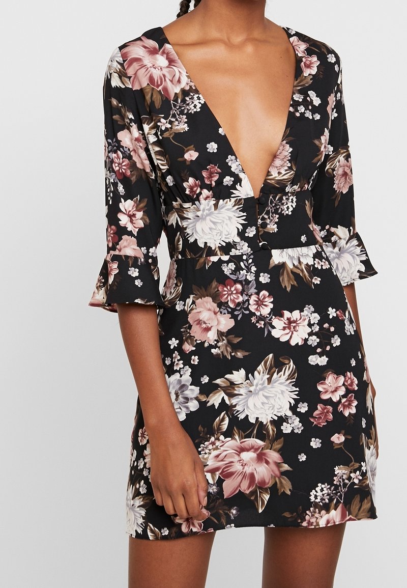 Robe noire avec un décolleté en V profond et des manches trois-quarts, présentant de grands motifs floraux roses, blancs et marron.