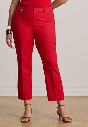 Mujer vestida con pantalones rojos de pierna recta, una blusa roja, sandalias marrones de tacón con tiras, y pulseras gruesas en la muñeca izquierda.