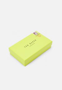 Scatola rettangolare Ted Baker, esterno giallo brillante e texturizzato, con il nome del marchio stampato in nero e un timbro decorativo sul coperchio.
