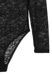 Body in pizzo nero con motivo floreale, maniche lunghe, aperture alte sulle gambe e bordi ondulati lungo il collo e le gambe.