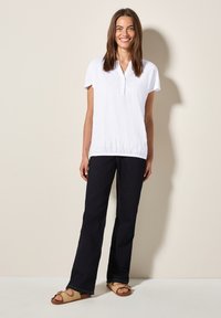 Witte top met korte mouwen, een kraag en een geplooid zoom, gecombineerd met donkerblauwe jeans en tan gekruiste sandalen. Eenvoudig ontwerp.