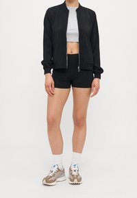 Black bomber jacket with silver zipper, grey crop top, black shorts, and beige sneakers with white accents. Solid colors and casual fit.