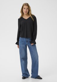 Black long-sleeve top with a V-neck, featuring gathered cuffs, paired with high-waisted wide-leg blue jeans and black shoes.