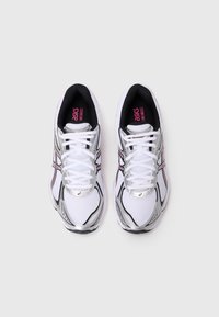 Scarpe sportive bianche con accenti argento e bordi neri, caratterizzate da materiale in rete, lacci piatti e una suola testurizzata pronunciata.
