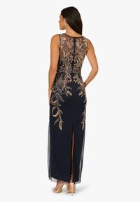 Marineblaues Kleid mit einem durchsichtigen, bestickten Rücken, der goldene Blumenmuster zeigt, und einem seitlichen Schlitz, ergänzt durch eine figurbetonte Silhouette und weiche Textur.