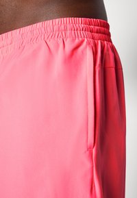 Rózsaszín sportshort, elasztikus derékkal, sima textúrával, oldalsó zsebekkel és diszkrét varrási részletekkel az illesztéseknél.