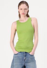 Green ribbed tank top with a rounded neckline and sleeveless design. Paired with loose blue denim jeans, showcasing a casual style.