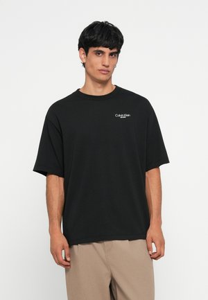 Black cotton t-shirt featuring a crew neck and short sleeves, with a white "Calvin Klein Jeans" logo on the left chest area.