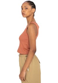 Rostfarvet, ribbet, ærmeløs crop top med tætsiddende design, parret med lys beige, løstsiddende bukser.