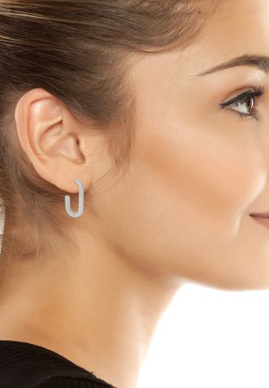 Orecchini in metallo argentato con design ad anello aperto, caratterizzati da una superficie liscia e da una forma minimalista, indossati all'orecchio di un modello.