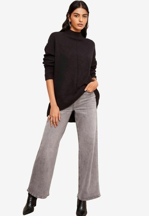 Schwarzer, übergroßer Rollkragenpullover mit gerippten Bündchen und Saum, kombiniert mit hellgrauen, weit geschnittenen Jeans und schwarzen Ankle-Boots.
