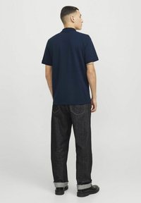Marineblå polo med korte ærmer, kombineret med mørke denim jeans. Sættet har en afslappet pasform og opfoldede manchetter, parret med sorte sko.