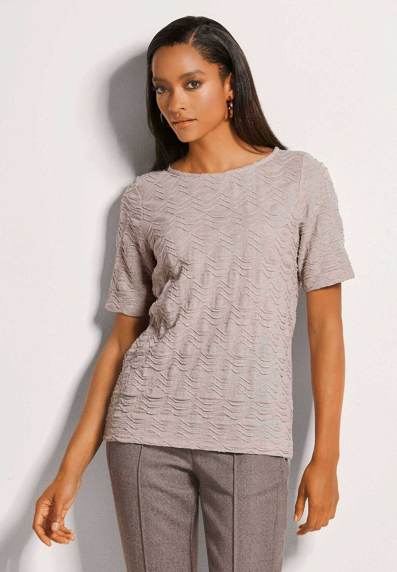 Helles beige Kurzarmhemd mit einem strukturierten wellenförmigen Muster, Rundhalsausschnitt und lockerer Passform. Kombiniert mit maßgeschneiderten braunen Hosen.