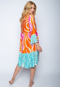 Kleurrijke jurk met gedurfde, draaiende patronen in oranje, roze en teal. Ontworpen met een gelaagde rok en klokvormige mouwen.