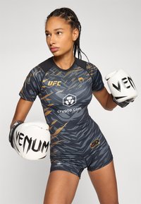 UFC kvinnelig kampdrakt, med en tilpasset grå og svart kamuflasjedesign med oransje detaljer, korte ermer og matchende shorts.