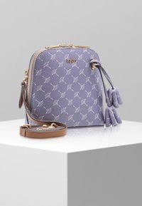 Fioletowa teksturowana torba z białym wzorem, złotymi okuciami, zapięciem na zamek błyskawiczny i ozdobnymi frędzlami. Posiada odpinany brązowy pasek.