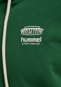 Grøn hættetrøje med hvid snøre, der har et hvidt hummel sportswear-logo og et stiliseret colosseum-design på brystet.