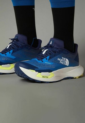 Zapatillas deportivas azules con parte superior de malla, detalles amarillos, suela intermedia blanca gruesa y suela exterior negra texturizada, etiquetadas como "THE NORTH FACE ENDURIS 4 VECTIV."