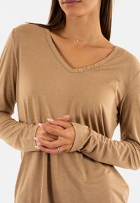 Lichtbruin shirt met lange mouwen en een V-halslijn, drie decoratieve knopen aan de voorkant en een zachte, gladde textuur.