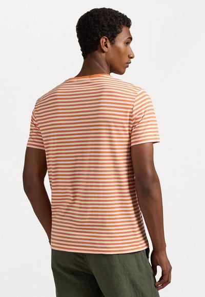 Πορτοκαλί και άσπρη ριγέ μπλούζα με κοντά μανίκια, στρογγυλή λαιμόκοψη, με χαλαρή εφαρμογή και μαλακή υφή. Φορεμένη με πράσινα παντελόνια.