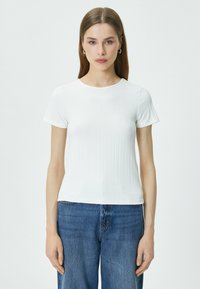 Hvid ribbet t-shirt med korte ærmer, rund halsudskæring, tætsiddende silhuet og glat tekstur, parret med blå denimjeans.