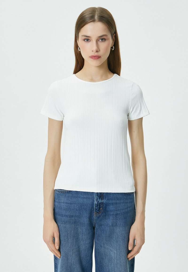 Hvid ribbet t-shirt med korte ærmer, rund halsudskæring, tætsiddende silhuet og glat tekstur, parret med blå denimjeans.