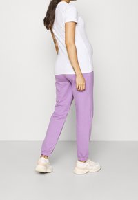 T-shirt blanc à manches courtes associé à un jogging lavande avec des poignets élastiques et une coupe décontractée. Le modèle porte des baskets claires.